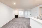 This single-floor residence offers a practical and comfortable layout across several thoughtfully designed areas. The spacious living room serves as the heart of the home, featuring plush wall-to-wall carpeting, a tile-surround fireplace as a focal point, recessed lighting, and a sliding glass door with vertical blinds that invites natural light and provides outdoor access. The open-concept kitchen flows seamlessly from the living area, separated by a peninsula countertop with an integrated sink — ideal for casual dining or meal prep. The kitchen is equipped with light wood cabinetry, a white electric range, a refrigerator, and tile flooring that contrasts cleanly with the carpeted areas. A dedicated entry area near the front door features recessed lighting and a closet, creating a welcoming transition into the home. The bedroom is generously sized with soft carpeting, large windows fitted with blinds that allow ample natural light, and a baseboard heater. A full bathroom completes the space, featuring tile flooring, a combined tub and shower with grab bars, and clean white fixtures throughout. The overall aesthetic is bright and neutral, with white walls and consistent finishes that offer a clean, move-in-ready canvas.