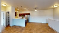 Located at 16511 East Sprague Avenue in Spokane Valley, WA, Unit 9 is a single-floor residence featuring a thoughtfully designed open-concept layout. The living and dining area flows seamlessly from the kitchen, unified by warm wood-look laminate flooring throughout the main living spaces. A peninsula counter with a crisp white surface serves as the central divider, providing both workspace and a casual dining option while maintaining the open feel of the space.

The kitchen is well-appointed with rich dark wood cabinetry, white countertops, a tile backsplash, and a full suite of stainless steel appliances including a refrigerator, stove, built-in microwave, and dishwasher. Pendant lighting above the kitchen area adds a modern accent. The galley-style kitchen corridor leads to a dedicated pantry or utility closet, adding practical storage.

The bedrooms feature plush carpeting and neutral tones, with at least one room offering a large window that allows ample natural light and views of the surrounding neighborhood. The full bathroom includes a single-sink vanity with dark wood cabinetry, a tiled backsplash accent, a large mirror, and a shower-tub combination. Baseboard heating is present throughout, and recessed and pendant lighting enhance the overall ambiance of this clean, move-in-ready residence.