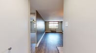 Located at 101 N Grant St in Denver's vibrant Capitol Hill neighborhood, this one-bedroom, one-bathroom unit offers a well-organized single-level layout that makes efficient use of its space. The open living area features light-toned hardwood-style flooring and neutral wall tones, creating a bright and clean atmosphere. A peninsula-style kitchen flows directly into the living space, equipped with warm wood cabinetry, black appliances including a refrigerator, range, and microwave, and a dark countertop that doubles as a breakfast bar — ideal for casual dining or meal prep. A hallway connects the main living area to the private quarters, providing a natural separation between spaces. The bedroom is a comfortable, well-proportioned room finished with plush carpeting, a ceiling fan, and a wall-mounted HVAC unit. Its wide sliding window frames views of the Denver cityscape, filling the room with natural light. The bathroom is finished with full beige tile surround in the tub-shower combination, accented by a decorative tile border and outfitted with stainless steel grab bars and a handheld showerhead for added accessibility. Clean white fixtures and neutral tones complete the bathroom's functional design. Overall, this unit offers a practical and comfortable urban living environment in the heart of Denver.