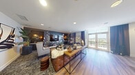 Located at 1640 East Sunrise Boulevard in Fort Lauderdale, FL, this thoughtfully designed single-floor space blends contemporary style with bold, artistic details. The combined kitchen and living area serves as the heart of the space, where wide-plank hardwood flooring flows seamlessly from the kitchen into the open living zone. The kitchen features dark navy cabinetry, a stainless steel refrigerator, and a peninsula bar counter topped with a sleek stone surface and accented by striking cluster pendant lights, providing casual seating for multiple guests.

The living area is defined by a dramatic botanical-themed feature wall in deep navy, adorned with a large-scale floral mural and a wall-mounted flat-screen television. Rich, patterned carpeting anchors the seating arrangement, which is complemented by curated artwork, lush indoor plants, and warm ambient lighting. Floor-to-ceiling windows and glass doors open to a private balcony, flooding the space with abundant natural light and offering views of the surrounding Fort Lauderdale skyline.

The bathroom continues the botanical theme with bold black-and-white floral wallcovering extending to the ceiling, paired with a floating stone vanity, a round mirror, and ADA-accessible fixtures. The hallway connects the spaces efficiently, completing this refined and cohesive layout.