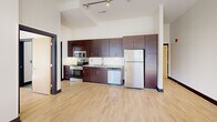 Located at 50 West Fourth Street in the heart of downtown Winston-Salem, this one-bedroom, one-bathroom apartment offers an efficient yet well-designed layout. Soaring ceilings and light hardwood flooring create an open, airy atmosphere throughout. The kitchen is outfitted with rich dark cabinetry, stainless steel appliances including a refrigerator, range, microwave, and dishwasher, complemented by track lighting overhead. The bedroom features a sliding wood-panel closet door with built-in shelving and a large window offering urban streetscape views. The bathroom includes a full soaking tub and a bright window overlooking the downtown streetscape. Large black-framed windows throughout flood the space with natural light.