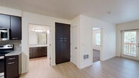This one-bedroom, one-bathroom apartment in Portland, Oregon offers a thoughtfully designed single-floor layout that makes efficient use of its compact footprint. The open kitchen is a standout feature, showcasing rich dark espresso cabinetry, granite-style countertops, a stone tile backsplash, and a full suite of stainless steel appliances including a refrigerator, range, microwave, and dishwasher. Light hardwood-style flooring runs throughout the kitchen and living areas, lending a bright, clean aesthetic. A tall pantry cabinet provides additional storage conveniently situated near the kitchen. The bedroom features plush wall-to-wall carpeting and a window offering a lush, green outdoor view, creating a calm and private retreat. A built-in closet with shelving and hanging space adds practical storage. The bathroom is clean and functional, featuring a full tub-shower combination, light hardwood-style flooring, a granite-topped vanity with dark cabinetry, and brushed nickel fixtures and grab bars. The overall design is modern and neutral throughout, with crisp white walls and consistent finishes that create a cohesive, move-in-ready living space.