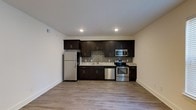 This single-floor, one-bedroom, one-bathroom unit offers a well-designed layout with modern finishes throughout. The kitchen serves as a standout feature, showcasing rich, dark espresso cabinetry that extends from base to upper cabinets, providing ample storage. Light-toned countertops offer a striking contrast to the cabinetry, while a mosaic tile backsplash adds a refined textural detail. The kitchen is fully equipped with a stainless steel appliance suite, including a refrigerator, electric range, built-in microwave, and dishwasher, making it both functional and visually cohesive. Recessed lighting illuminates the space efficiently, highlighting the clean lines and contemporary aesthetic. Light-toned, hardwood-style flooring runs throughout, lending warmth and continuity to the space. Neutral wall tones complement the overall design palette, creating a bright and inviting atmosphere. The open arrangement of the kitchen and living area contributes to an efficient and comfortable flow, making practical use of the available space. This unit combines modern design elements with functional features to create a well-appointed living environment.