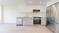 Located at 2453 Renfrew St in Vancouver, BC, this well-appointed one-bedroom, one-bathroom unit offers a thoughtfully designed layout across a single floor. Light-toned luxury vinyl plank flooring flows throughout, lending a clean, modern aesthetic to the entire space.

The kitchen is a standout feature, outfitted with flat-panel white cabinetry extending to the ceiling, quartz countertops with a marble-inspired backsplash, and a full suite of stainless steel appliances including a refrigerator, range, over-the-range microwave, and dishwasher. Recessed lighting and an open sightline toward the hallway give the kitchen an airy, functional feel.

The bedroom is a comfortable retreat, bathed in natural light from a large window offering outward views of the surrounding neighbourhood. It connects directly to a dedicated walk-in closet, complete with wire shelving for organized storage.

The bathroom is finished to a high standard, featuring large-format stone-look tiles on both the floor and tub surround, a soaker tub with a curved shower rod, and a sleek white floating vanity with quartz countertop and black hardware accents. Recessed lighting enhances the spa-like atmosphere.

Warm, neutral tones and clean lines are carried throughout the unit, creating a cohesive and contemporary living environment.
