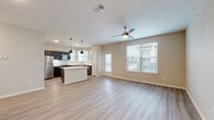 This single-floor residence showcases a thoughtfully designed open-concept layout that seamlessly connects the living area and kitchen. The living space is finished with light hardwood-style flooring throughout and features a ceiling fan with lighting, a large window dressed with blinds that allows natural light to fill the room, and a glass door providing access to an outdoor area. The kitchen is well-equipped with dark espresso cabinetry, white quartz countertops, a full suite of stainless steel appliances including a refrigerator, range, built-in microwave, and dishwasher, complemented by a tiled backsplash and stylish pendant lighting hanging above a central island. The bedroom offers plush carpeting, a ceiling fan, recessed lighting, and a window overlooking the surrounding area. The bathroom includes a wide white quartz vanity with an undermount sink, dark cabinetry for storage, a large mirror, and a walk-in shower with a glass enclosure. Throughout the unit, neutral warm-toned walls, consistent finishes, and clean architectural lines create a cohesive and inviting atmosphere suited to modern living.