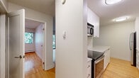 This efficiently laid-out one-bedroom, one-bathroom unit offers a clean, neutral aesthetic throughout its single floor. Warm hardwood flooring flows seamlessly through the living room, hallway, and bedroom, creating a cohesive and inviting atmosphere.

The kitchen is neatly arranged with white shaker-style cabinetry extending to the ceiling, providing ample storage. Stainless steel appliances, including a built-in microwave and electric range, complement the light countertops, giving the kitchen a modern and functional character.

The living room benefits from a large window that frames views of lush greenery, filling the space with natural light. A baseboard heating system runs along the perimeter, ensuring comfortable warmth throughout the unit.

The bedroom is a well-proportioned retreat with a sliding closet, light-toned walls, and a window overlooking leafy outdoor scenery. Baseboard heating is also present, adding to the room's comfort.

The bathroom features hardwood-style flooring, a white vanity with a stone-look countertop, a medicine cabinet, and clean white walls, offering a simple yet functional design.

A connecting hallway ties all rooms together efficiently, making the overall layout practical and easy to navigate. The unit's consistent white walls and warm wood tones create a bright, clean, and move-in-ready living space.