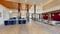 This expansive single-floor community clubhouse offers a thoughtfully designed, multi-functional space that blends sophisticated aesthetics with practical amenities. The grand lobby serves as the centerpiece, showcasing soaring double-height ceilings, striking wood-slat architectural details, reclaimed dark wood columns, and light hardwood flooring interspersed with brick tile inlays. A curved front desk with bold navy velvet seating sets a polished, welcoming tone, while a secondary lounge nook with crimson upholstered seating adds a vibrant contrast.

The dining area is adorned with eye-catching star-patterned encaustic tile flooring, a round dark-topped table with white and gold-accented chairs, and floor-to-ceiling windows that flood the room with natural light and outdoor views. Adjacent, the kitchen features a long white quartz island with gold-framed barstools, glossy white vertical tile backsplash, warm wood accents, and elegant floral pendant lighting. A dedicated workspace area includes hexagonal burgundy tile accents and built-in workstations.

The game and living room area offers a full-size billiard table set against a dramatic stacked-stone accent wall with a wall-mounted TV and warm sconce lighting. A dedicated package locker room provides convenient secure storage. The space also includes access to a garage, completing this well-rounded, amenity-rich facility.