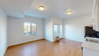 Located at 7550 N Lombard St in Portland's St. Johns neighborhood, Unit 201 is a thoughtfully designed second-floor residence that combines functional layout with clean, contemporary finishes throughout. Warm hardwood-style flooring flows continuously across the entire unit, creating a cohesive and inviting atmosphere from room to room.

The open living area is bathed in natural light courtesy of large windows that frame views of the surrounding neighborhood. A glazed entry door adds additional brightness to the space, while a wall-mounted HVAC unit ensures year-round climate control. The clean white walls and flush-mount lighting contribute to the unit's bright, airy feel.

The kitchen features a two-tone cabinet design — crisp white uppers paired with light blue lower cabinets — accented by a classic white subway tile backsplash. Stainless steel appliances, including a refrigerator and electric range with hood, complement the light countertops and single-basin sink, creating a practical and stylish cooking space.

The bathroom is finished with full white subway tile surrounding the soaking tub and shower, lending a timeless, clean aesthetic. A dedicated laundry area accommodates a stacked washer and dryer unit, conveniently tucked behind louvered doors in the hallway. Additional closet storage is also present along the corridor, maximizing the unit's organizational capacity.