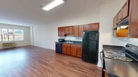 This single-floor residence at 255 E Grand Ave in Rahway, NJ offers a practical and well-designed layout encompassing one bedroom, a den, two full bathrooms, and a combined dining and living area. Rich hardwood-style flooring flows consistently throughout the space, creating a warm and cohesive aesthetic. The kitchen is a standout feature, outfitted with rich cherry wood cabinetry, dark countertops, a mosaic tile backsplash, and a full suite of black appliances including a refrigerator, electric range, dishwasher, and microwave. Generous cabinet storage and ample counter space make it highly functional. The open living and dining area is bright and airy, with neutral white walls and a large window in the bedroom that brings in natural light and exterior views. The primary bedroom provides a comfortable retreat with dedicated closet space. The den offers flexible space suitable for a home office or additional living area. Both bathrooms are finished with light tile flooring and warm wood vanities — one featuring a tub/shower combination and the other a walk-in glass shower. Two closets provide additional storage throughout. The entrance leads conveniently into the main living area, and the overall layout promotes a smooth, connected flow between all rooms.