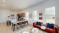 Located at 11110 Lantern Rd in Fishers, Indiana, this well-appointed 1-bedroom, 2-bathroom residence offers a thoughtfully designed single-floor layout that maximizes every square foot. The open-concept living, dining, and kitchen area forms the heart of the home, anchored by a striking quartz waterfall island with bar seating and a deep undermount sink. The kitchen features rich dark wood cabinetry extending to the ceiling, stainless steel appliances including a refrigerator, range, and built-in microwave, complemented by a tile backsplash and pendant globe lighting that adds a warm, modern touch. Soaring ceilings throughout the main living area create an airy, expansive feel, enhanced by large windows that flood the space with natural light. The living room offers generous proportions with views of the outdoors through a bank of windows dressed with layered blinds and floor-to-ceiling drapes. Light wood-style flooring runs throughout the main areas, transitioning to plush carpet in the private bedroom, which includes a large window and dedicated closet. Both bathrooms are finished with dark wood vanities, white quartz countertops, and wood-look flooring. Built-in shelving adds functional character to the living area, completing this polished and cohesive home.