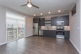 This single-floor unit offers a cohesive, contemporary design highlighted by wood-look flooring that flows seamlessly throughout every room. The kitchen is a standout feature, outfitted with dark two-tone cabinetry in navy and espresso tones, a light quartz countertop, a subway tile backsplash, and a full suite of stainless steel appliances including a refrigerator, dishwasher, microwave, and range. Recessed lighting illuminates the space, while a sliding door opens directly onto a private balcony with metal railing, allowing natural light to fill the kitchen and adjacent living area. The entry hallway is clean and well-proportioned, with tall white baseboards, neutral beige walls, a wall-mounted thermostat, and a solid white paneled front door. Rooms throughout maintain the same warm, neutral tones and consistent flooring, creating a unified aesthetic. A spacious bedroom features wide walls and a window, offering a bright, versatile layout. Overall, the unit presents a polished, move-in-ready environment with modern finishes and a functional, open feel.