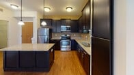 Located at 20 Sixth St NW in Osseo, Minnesota, this single-floor residence offers a thoughtfully designed layout with modern finishes throughout. The kitchen serves as a centerpiece of the home, showcasing rich dark cabinetry, gleaming granite countertops, a central island with pendant lighting, and a full suite of stainless steel appliances including a refrigerator, range, and microwave. Wood-look flooring runs through the kitchen and living areas, adding warmth and continuity to the open-concept space. A sliding glass door floods the living area with natural light and provides outdoor access. The bedrooms are carpeted for comfort and feature neutral, earthy tones with ample closet space and windows that bring in additional natural light. Two bathrooms mirror the kitchen's refined aesthetic, each featuring granite-topped dark vanities and wood-look flooring; one includes a shower-tub combination. A dedicated in-unit laundry area with side-by-side washer and dryer and built-in shelving adds everyday convenience. The overall ambiance is clean, contemporary, and functional, making this Osseo residence a practical and stylish place to call home.