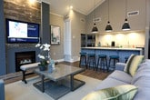 Located at 550 St. Michaels Way in Newport News, Virginia, this single-floor clubhouse or community space is designed to impress with its open, airy layout and sophisticated interior finishes. The space is anchored by a dramatic lounge area featuring soaring vaulted ceilings clad in shiplap, a stone-accented fireplace with a mounted flat-screen television, and an array of large arched and grid-pane windows that flood the interior with abundant natural light and provide sweeping views of the surrounding landscape. Rich hardwood-style flooring runs throughout, complementing the cool gray and blue tones of the walls and furnishings.

A well-appointed kitchen serves as a central hub, boasting granite countertops, a generous island with teal bar stool seating, stainless steel appliances, and stylish matte black pendant lighting that hangs dramatically from the vaulted ceiling. The kitchen opens seamlessly into the main gathering area, reinforcing the space's open-plan design.

A welcoming entry foyer features tasteful accent seating, a large mirror, and direct access to the outdoors through a glass-paned door. Throughout the space, the interplay of high ceilings, generous windows, warm flooring, and curated furnishings creates a bright, refined atmosphere well-suited for community gatherings and social events.