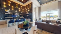 Located at 7200 N 91st Ave in Glendale, Arizona, this single-floor community lounge space delivers a sophisticated and welcoming atmosphere through a thoughtful blend of modern design and functional amenities. The space is divided into two seamlessly connected areas: a fully appointed kitchen and an expansive living room.

The kitchen area is a standout feature, showcasing rich, dark geometric-patterned tile walls that serve as a dramatic backdrop to warm wood cabinetry and granite-style countertops. Floating wood shelves display curated décor, while cascading Edison-style pendant lights create an ambient glow. A built-in coffee station and bar seating with woven blue chairs add both practicality and style.

The living room is equally impressive, anchored by a large sectional sofa and a wall-mounted flat-screen television recessed into a textured accent wall. A decorative coffered ceiling detail with a dark tile inlay adds architectural depth overhead, while floor-to-ceiling windows flood the space with natural light and provide views of the surrounding exterior. Built-in shelving and a mezzanine-level railing visible above contribute to the sense of vertical volume.

A wide corridor with textured wall panels, curated artwork, and modern bench seating provides a polished transitional entry to the space. Throughout, large-format tile flooring ties all areas together cohesively, reinforcing the upscale, contemporary character of this communal lounge.