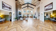 Located at 8811 31st Ave NE in Lacey, Washington, this single-floor community clubhouse offers a spacious and thoughtfully curated environment spanning a generous footprint. The grand lobby serves as the heart of the facility, showcasing soaring vaulted ceilings with dramatic exposed dark wood beams, elegant hoop chandeliers, and herringbone-patterned wood flooring. Shiplap-clad walls contribute a modern farmhouse aesthetic throughout, while large windows and glass doors flood the space with abundant natural light.

A welcoming reception area greets visitors with warm leather seating and tall shiplap walls accented by scenic Pacific Northwest artwork. A stylized corridor features a vintage Honda motorcycle on display, blending artistic flair with eclectic character. The clubroom and lounge areas provide comfortable gathering spaces, one of which includes a pool table surrounded by floor-to-ceiling windows overlooking outdoor amenities.

A bright café-style dining area offers a distinctive inlaid tile-and-wood floor, globe pendant lighting, and walls adorned with botanical prints. The fitness center is a standout amenity, featuring vaulted ceilings with exposed beams, sports-themed wall art, a full suite of cardio and strength equipment, rubberized flooring, and large mirrors. An adjoining functional training area provides additional workout versatility. Together, these spaces create a cohesive, design-forward community hub.