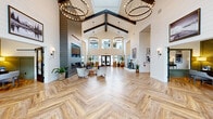 Located at 8811 31st Ave NE in Lacey, Washington, this single-floor community clubhouse offers a spacious and thoughtfully curated environment spanning a generous footprint. The grand lobby serves as the heart of the facility, showcasing soaring vaulted ceilings with dramatic exposed dark wood beams, elegant hoop chandeliers, and herringbone-patterned wood flooring. Shiplap-clad walls contribute a modern farmhouse aesthetic throughout, while large windows and glass doors flood the space with abundant natural light.

A welcoming reception area greets visitors with warm leather seating and tall shiplap walls accented by scenic Pacific Northwest artwork. A stylized corridor features a vintage Honda motorcycle on display, blending artistic flair with eclectic character. The clubroom and lounge areas provide comfortable gathering spaces, one of which includes a pool table surrounded by floor-to-ceiling windows overlooking outdoor amenities.

A bright café-style dining area offers a distinctive inlaid tile-and-wood floor, globe pendant lighting, and walls adorned with botanical prints. The fitness center is a standout amenity, featuring vaulted ceilings with exposed beams, sports-themed wall art, a full suite of cardio and strength equipment, rubberized flooring, and large mirrors. An adjoining functional training area provides additional workout versatility. Together, these spaces create a cohesive, design-forward community hub.
