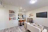 Located at 775 S Belmont St in Delano, CA, this thoughtfully designed one-bedroom, one-bathroom residence offers a clean, modern aesthetic across a single floor. The open-concept living, dining, and kitchen area creates a seamless flow, anchored by light wood-look flooring and bright white walls that maximize the sense of space. The living room features a window that invites natural light, while a wall-mounted TV and comfortable seating make it an inviting space to relax.

The kitchen is well-appointed with light wood cabinetry, crisp white countertops, stainless steel appliances including a French door refrigerator, gas range, dishwasher, and built-in microwave. A peninsula with bar seating connects the kitchen to the dining area, which comfortably accommodates a small dining set.

The generously sized bedroom is carpeted for comfort and includes a ceiling fan, a window with natural light, and a wall-mounted TV. A walk-in closet with wrap-around shelving and hanging rods offers ample storage. The full bathroom features wood-look tile flooring, a vanity with wood-tone cabinetry, and a tub-shower combination. A hallway connects all rooms, completing this efficient and stylish layout.