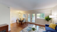 This thoughtfully designed single-floor residence offers two bedrooms and one bathroom across a comfortable and efficiently laid-out floor plan. Warm hardwood flooring runs throughout the entire space, lending a cohesive and inviting feel to every room.

The living room is bright and welcoming, featuring large windows and a glass door that fill the space with abundant natural light and offer views of lush greenery outdoors. The adjoining dining area continues the open feel, highlighted by a pendant light fixture and a window overlooking the tree-lined exterior. Together, these spaces create a seamless flow ideal for both everyday living and entertaining.

The kitchen is clean and modern, outfitted with white shaker-style cabinetry, white subway tile backsplash, quartz countertops, and a full suite of stainless steel appliances including a refrigerator, range, microwave, and dishwasher. A kitchen island provides additional prep and counter space.

The primary bedroom is generously sized, offering a closet and hardwood flooring, while the second bedroom features a window with garden views and its own closet. The shared bathroom includes a combination tub and shower with grab bars and a handheld showerhead. Clean, neutral tones throughout the space create a calm and functional living environment.
