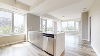 Located on Wellington Street West in Ottawa's vibrant Hintonburg neighbourhood, this modern 2-bedroom, 2-bathroom unit offers a well-designed open-concept layout with contemporary finishes throughout. Light wood-tone laminate flooring runs continuously across the space, complementing the neutral warm-grey palette on the walls.

The combined kitchen and living area forms the heart of the unit. The kitchen features a large central island with a wood-grain finish and integrated sink, stainless steel appliances including a refrigerator, stove, and built-in microwave, white subway tile backsplash, and ample upper and lower cabinetry. Floor-to-ceiling windows in the living area flood the space with natural light and frame expansive city views of the Ottawa skyline and surrounding greenery.

A clean, well-lit hallway connects the bedrooms and bathrooms. Both bedrooms are generously proportioned with large windows offering city views, neutral toned walls, and hardwood-style flooring. The primary bedroom includes a sliding-door closet and access to a dedicated bathroom. A second full bathroom features a glass-enclosed walk-in shower with white horizontal tile surround and polished chrome fixtures.

The unit also includes a dedicated closet, providing practical storage. The overall ambiance is bright, clean, and modern, ideal for urban living.