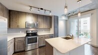 Located at 425 N Boylan Avenue in Raleigh, NC, this one-bedroom, one-bathroom residence offers a well-designed layout with modern finishes and industrial-inspired architectural details. The open-concept kitchen and living area serves as the heart of the home, featuring rich wood-toned cabinetry extending to the ceiling, stainless steel appliances including a refrigerator, electric range, and microwave, and a large kitchen island with a white quartz countertop and undermount sink. Track lighting and elegant pendant fixtures illuminate the space, which flows directly onto a private balcony through a sliding glass door. The bedroom offers exposed concrete ceiling detail, dark hardwood-style flooring, a ceiling fan, and a natural light-filled window with exterior views. A walk-in closet provides generous storage. The bathroom is finished with large-format tile in the tub/shower surround, light tile flooring, a wood-framed vanity mirror, and clean white fixtures. A dedicated laundry room houses a full-size side-by-side washer and dryer. Throughout the residence, dark hardwood-style flooring, exposed concrete ceiling elements, and crisp white walls create a contemporary urban aesthetic that blends industrial character with refined comfort.