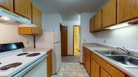 Located at 3131 N Squirrel Rd in Auburn Hills, Michigan, this single-floor unit offers a straightforward and functional layout designed for comfortable everyday living. The galley-style kitchen is well-equipped with warm oak cabinetry lining both sides, providing ample upper and lower storage. It includes a white electric range with overhead ventilation, a full-size refrigerator, and a double sink with countertop workspace. Light tile flooring runs throughout the kitchen, which opens toward a hallway connecting the rest of the unit. The living and dining areas feature neutral wall-to-wall carpeting and are brightened by a classic brass chandelier, adding a touch of warmth to the open space. Baseboard heating lines the perimeter, ensuring year-round comfort. The bedroom includes a generously sized closet with bi-fold doors and a full-width hanging rod for organized storage, also finished with soft carpet underfoot. The bathroom is clean and practical, featuring tile flooring, a single-sink vanity with wood cabinetry, a wall mirror with overhead lighting, and a dedicated walk-in shower stall with tile surround. An entry closet near the front door offers additional storage, completing the efficient and livable floor plan of this Auburn Hills residence.