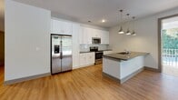 Located on Maybank Highway in Charleston, South Carolina, this single-floor residence offers a thoughtfully designed open-concept layout with modern finishes throughout. The kitchen serves as the centerpiece of the main living area, showcasing white shaker-style cabinetry, dark quartz countertops, a subway tile backsplash, and a full suite of stainless steel appliances including a French door refrigerator, range, and microwave. A generous kitchen island with an integrated sink and pendant lighting provides additional workspace and separates the kitchen from the expansive living area. The living space features warm hardwood-style flooring, a ceiling fan, and large windows with blinds that allow for abundant natural light and views of surrounding greenery. A sliding glass door connects the main living area to the outdoors. The bedrooms are carpeted for comfort, each equipped with ceiling fans, built-in shelving, and windows overlooking the lush exterior. The primary bathroom offers a dual-sink vanity with white cabinetry, dark countertops, and hardwood-style flooring. A secondary bathroom features a full tub-shower combination with clean white tile surrounds. Built-in shelving units in the bedrooms provide practical storage solutions, completing this well-appointed Charleston residence.