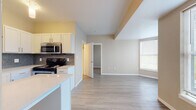 Located at 19752 Pikes Peak Ave in Parker, Colorado, this single-floor unit offers a well-designed, open-concept layout with modern finishes and functional living spaces. Light-toned luxury vinyl plank flooring runs throughout, creating a cohesive and easy-to-maintain foundation across every room.

The kitchen is a standout feature, equipped with white shaker-style cabinetry, light quartz countertops, and a striking gray subway tile backsplash. Stainless steel appliances—including a refrigerator, electric range with microwave above, and dishwasher—complete the space. A peninsula with additional cabinetry provides extra prep area and casual seating potential, while a pendant light adds a decorative touch.

The kitchen opens seamlessly into the living area, which benefits from a curved bay window arrangement that draws in generous natural light and provides views of the surrounding neighborhood. Warm neutral tones on the walls complement the overall brightness of the space.

A dedicated hallway leads to the bathroom, which features a full soaking tub with a clean white tile surround and chrome fixtures. Adjacent to the bedroom area, an in-unit laundry alcove houses a stacked washer and dryer alongside a walk-in closet with built-in shelving, adding significant everyday convenience to the layout.