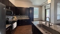 This well-appointed 1,090 square foot residence in Sandy, Utah offers 2 bedrooms and 2 bathrooms across a single floor, designed with modern finishes throughout. The open kitchen is a standout feature, showcasing dark espresso cabinetry, granite countertops, a tile mosaic backsplash, stainless steel appliances, a central island with a undermount sink, and rich hardwood-style flooring. Track lighting and abundant natural light from a large window enhance the kitchen's functional appeal. The living room continues the hardwood-style flooring and features a curved wall with a bay of large windows and a ceiling fan, creating a bright, airy atmosphere. The primary bedroom measures 240 square feet and is carpeted with dual windows admitting natural light. The second bedroom also features carpet flooring, a ceiling fan, and a window with outdoor views. Both bathrooms are finished with large-format tile flooring, dark vanity cabinetry, granite countertops, and framed mirrors. The primary bath includes a walk-in shower and a dual-vanity setup, while the secondary bath features a full tub-shower combination. A hallway connects all rooms, completing this cohesive and stylishly finished floor plan.