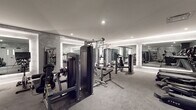 Located at 1 Atlantic St in Stamford, Connecticut, this single-floor fitness center offers a comprehensively equipped workout facility with a sleek, modern aesthetic. The space is finished throughout in a cohesive gray palette, featuring textured concrete-style walls, gray rubberized flooring, and a white ceiling with recessed lighting that creates a clean, professional atmosphere.

The facility is divided into distinct functional zones. A strength training area houses multiple True-brand cable and resistance machines alongside free weights, dumbbells, and balance training equipment such as a BOSU ball. A dedicated cardio section features a lineup of elliptical trainers, treadmills, stair climbers, and a rowing machine with an integrated monitor.

Large mirrors framed by continuous LED strip lighting are positioned throughout the space, visually expanding the room and providing users with clear sightlines during workouts. The illuminated mirror frames serve as a key architectural detail, lending the space an upscale, boutique-gym quality.

The layout is open and well-organized, allowing for comfortable movement between equipment zones. The space is accessed through a set of white double doors and benefits from a well-ventilated ceiling system. Overall, the fitness center combines functional design with refined finishes to deliver a high-quality workout environment.