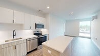 This thoughtfully designed 2-bedroom, 2-bathroom residence at 108 Hamilton St in Bound Brook, NJ offers a clean, modern aesthetic throughout its single-floor layout. The open-concept kitchen and living area serves as the heart of the home, anchored by a large central island with a sleek white countertop and warm wood-toned base. The kitchen is outfitted with full stainless steel appliances, including a French door refrigerator, electric range, over-the-range microwave, and dishwasher, complemented by two-tone cabinetry featuring white upper cabinets and natural wood lower cabinets with matte black hardware. Light wood-style flooring runs throughout the home, enhancing the bright, airy feel created by white walls and recessed lighting. Both bedrooms are generously proportioned, each equipped with a wall-mounted mini-split HVAC unit for individual climate control. The primary bedroom benefits from a large window with outdoor views. The two bathrooms showcase contemporary finishes, with one featuring a tiled tub/shower combo with matte black fixtures, and the other a glass-enclosed walk-in shower with a built-in niche. Additional conveniences include in-unit laundry, a utility room, and multiple closets for ample storage.