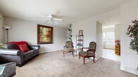 Located at 1114 SE Powell St in Topeka, Kansas, this two-story home offers a well-organized layout spread across two floors, accommodating two bedrooms, two bathrooms, a living room, dining room, office, and hallway. The entry foyer welcomes visitors with warm neutral tones, plush carpeting, and a bold dark front door flanked by a sidelight window. The living room is generously sized, featuring ceiling fans with light fixtures, soft carpet flooring, and windows that allow natural light to fill the space. The kitchen is equipped with warm oak cabinetry, a gas range, refrigerator, and ample counter space, flowing naturally into the bright dining area. The dining space benefits from a sliding glass door and windows overlooking a fenced outdoor area, creating an airy, connected feel. Both bedrooms are carpeted and include ceiling fans, natural light from windows, and closet storage — the primary bedroom offering a notably spacious footprint. The dedicated office provides a quiet, carpeted retreat with its own ceiling fan. The two bathrooms feature tile flooring and clean, functional finishes. Neutral wall tones and consistent carpeting throughout lend a cohesive, comfortable ambiance to the entire home.