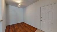 This single-floor unit offers a clean, functional layout with a welcoming entry that transitions seamlessly into an open living area. Rich, warm-toned hardwood floors extend throughout the main living spaces, complementing the crisp white walls and creating a bright, inviting atmosphere. Track lighting near the entry adds focused illumination, while a ceiling-mounted light fixture anchors the central living area.

The kitchen is well-appointed with honey-toned wood cabinetry providing generous storage, light-colored countertops, a full suite of appliances including a refrigerator, electric range, and dishwasher, and light tile flooring. A pass-through counter connects the kitchen to the adjacent dining or living area, enhancing the open flow of the space.

A dedicated bedroom features plush carpet flooring and a large window that frames outdoor greenery, filling the room with natural light. The full bathroom is outfitted with a wood vanity, a wide mirror, and a shower-tub combination, with hardwood flooring adding warmth to the space.

Throughout the unit, white walls and clean lines contribute to a neutral, versatile aesthetic, while the mix of hardwood and carpet flooring delineates each functional zone. The overall ambiance is practical and comfortable, offering a well-organized living environment.