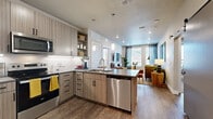 This thoughtfully designed two-bedroom, four-bathroom residence offers a contemporary open-concept layout across a single floor. The kitchen serves as a central hub, featuring stainless steel appliances including a side-by-side refrigerator, range, microwave, and dishwasher. Sleek wood-toned cabinetry with matte black hardware, a subway tile backsplash, and pendant lighting over the peninsula create a polished, functional workspace that flows seamlessly into the living area. The living room benefits from large windows that invite abundant natural light, complemented by wood-style plank flooring throughout the main areas.

Both bedrooms are carpeted and receive generous natural light through large windows. Each bedroom connects to its own dedicated bathroom, and both feature well-organized walk-in closets equipped with wire shelving, hanging rods, and built-in storage shelves. The bathrooms are finished with wood-toned vanities, undermount sinks, and grey countertops. One bathroom includes a soaking tub with full subway tile surround, while another features a glass-enclosed shower. A hallway connects the private areas of the residence, maintaining a clean, efficient flow throughout the home.