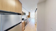 Located in Seattle's Ballard neighborhood, Unit 416 at 1140 NW Market St is a thoughtfully designed studio offering an efficient and modern living experience. The open layout is anchored by light-toned hardwood flooring that runs throughout, creating a warm and cohesive aesthetic.

The galley-style kitchen is well-appointed with white upper cabinetry, natural wood lower cabinets and tall pantry storage, a white tile backsplash, stainless steel appliances including an electric range, built-in microwave, and dishwasher, complemented by matte black fixtures at the sink — a refined contrast against the clean, contemporary finishes.

The main living area benefits from a striking corner window configuration, with large, floor-to-ceiling windows that flood the space with natural light and offer open views of the surrounding Ballard streetscape and neighborhood buildings. The bright, airy atmosphere is further enhanced by white walls and recessed lighting.

The bathroom features a fully tiled walk-in shower with vertically stacked cream-toned tile and matte black hardware, contributing a clean, modern feel. The overall design of the unit balances compact efficiency with high-quality finishes, making it a functional and stylish space in one of Seattle's most vibrant urban neighborhoods.