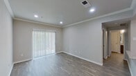 This single-floor residence offers a clean, modern aesthetic defined by neutral gray tones, crown molding, and consistent wood-look flooring throughout the main living areas. The living room is bright and welcoming, featuring recessed lighting, crisp white baseboards, and a large sliding glass door fitted with vertical blinds that invite natural light and provide access to the outdoors. The front entry opens into this living space, anchored by a classic six-panel white door and seamlessly flowing into the adjacent dining area. The kitchen is well-equipped with dark cabinetry, stainless steel appliances including a range and refrigerator, a built-in microwave, and a peninsula counter topped with granite-style surfaces and a stainless steel sink. The bedrooms are carpeted for comfort, with one featuring a ceiling fan with light fixture and a window with exterior views, while another offers a more private, quiet layout. The bathroom is neatly finished with dark vanity cabinetry, a granite-style countertop, a tub-shower combination, and wood-look flooring that ties the space together. Throughout, the unit presents a move-in-ready, cohesive design with practical finishes and a functional, efficient layout.