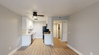 This well-appointed single-floor unit offers a cohesive, modern aesthetic throughout, characterized by a neutral gray-and-white color palette, clean lines, and quality finishes. The open living area is finished with light-toned luxury vinyl plank flooring and features a sliding glass door alongside a window that invites natural light and garden views, creating a bright and airy atmosphere.

The kitchen is efficiently designed with white shaker-style cabinetry accented by matte black hardware, light quartz countertops, and a stainless steel sink. Black appliances — including a refrigerator, range, and microwave — add a contemporary contrast. A ceiling fan with an integrated light fixture provides both comfort and illumination, while the open sightline to the hallway enhances the sense of connectivity throughout the space.

The bedrooms are finished with plush carpet and feature large sliding-panel closets with built-in hanging rods, offering practical storage. Each bedroom benefits from windows overlooking lush greenery, ensuring a calm and pleasant environment.

Two bathrooms serve the unit: one with a glass-enclosed walk-in shower, round mirror, and matte black fixtures, and a second with vinyl plank flooring, a white vanity, and matte black hardware accents. Both bathrooms maintain the clean, minimalist aesthetic found throughout the space.