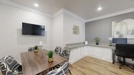 Located at 3331 Luella Blvd in La Porte, Texas, this single-floor space is thoughtfully designed to serve as both a collaborative meeting area and a comfortable work lounge. The layout comprises a dining room and a living room, each with its own distinct character while sharing a cohesive, contemporary aesthetic.

The dining room serves as the centerpiece of the space, featuring a rich wood-toned table surrounded by stylish gray patterned upholstered chairs. A wall-mounted flat-screen TV anchors one wall, while decorative artwork adds visual interest. A granite-topped built-in cabinet with white cabinetry lines one side of the room, offering both function and elegance. Crown molding and recessed lighting contribute to a polished, refined atmosphere, and wood-look plank flooring runs throughout, adding warmth underfoot.

The living area doubles as a functional workstation, equipped with a granite-topped desk accommodating multiple monitors and ergonomic seating. A bright window dressed with patterned curtains allows natural light to fill the room. A bold yellow tufted sofa paired with a gray ottoman and a striking large-scale abstract wall painting infuse the space with a vibrant, creative energy. Crown molding and neutral gray walls maintain a consistent, professional tone throughout. Together, the two areas create a versatile, inviting environment ideal for meetings, focused work, or relaxed collaboration.