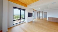 Bakers Place #1401 is a thoughtfully designed 1,490 sq ft condominium in Madison, WI, offering three bedrooms, three bathrooms, and a seamless open-concept layout. The kitchen is a standout feature, showcasing flat-panel light wood cabinetry, a large waterfall-edge island with an undermount sink and matte black fixtures, white quartz countertops, a built-in double wall oven, an induction cooktop, and a sleek wall-mounted range hood — all set above light hardwood flooring that flows throughout the unit. The living area features exposed wood beam ceilings and large black-framed windows that frame panoramic views of Madison's skyline and lake, filling the space with natural light. A built-in fireplace and open shelving add both function and character. The primary bedroom, at 190 sq ft, includes lake and city views, while all bedrooms benefit from the same warm wood beam accents. The bathrooms are finished with dark vertically stacked tile surrounds, soaking tubs, and matte black hardware. A well-organized walk-in closet with custom shelving, drawers, and rail systems provides ample storage. The unit's clean, minimalist aesthetic is consistent throughout, with white walls, light wood floors, and black hardware accents defining its modern character.