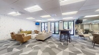 Located at 300 W Palmetto Park Rd in Boca Raton, Florida, this single-floor amenity space offers a thoughtfully designed environment with multiple distinct functional zones. The interiors are unified by a bold geometric-patterned carpet in tones of gray and white, providing a modern foundation throughout the common areas.

The main lounge area is generously proportioned, furnished with a mix of plush sofas, leather armchairs, and high-top bar seating. A decorative accent wall featuring a colorful speckled pattern adds visual interest, while large glass doors open to an outdoor balcony, filling the space with natural light and views of tropical landscaping. Full-wall mirrors in select areas amplify the sense of openness.

A dedicated screening room offers leather recliner seating, bean bag chairs, a projection screen, and acoustic wall panels, creating an intimate cinematic atmosphere. A separate conference-style area provides a formal meeting setup with upholstered seating around a central table.

A mezzanine level features rich hardwood flooring, elegant black-metal railings with decorative cross detailing, and a row of arched windows that flood the upper level with abundant natural light, adding architectural character to the overall space.