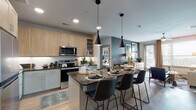 This single-floor residence showcases a thoughtfully designed open-concept layout that seamlessly connects the kitchen, dining, and living areas. The kitchen is a standout feature, equipped with stainless steel appliances including a French door refrigerator, electric range, and built-in microwave. Light wood cabinetry with glass-front upper cabinets lines the walls, complemented by dark granite countertops and a white subway tile backsplash. A central island with seating for multiple guests serves as both a functional workspace and casual dining area, illuminated by striking black pendant lights. Light hardwood flooring flows throughout the main living spaces.

The living room offers a comfortable, well-lit setting with large windows that allow natural light to fill the space, a ceiling fan, and a bold accent wall in deep charcoal.

Two bedrooms provide distinct character: one features a rich green accent wall with pattern drapery and generous natural light, while the second presents a warm, neutral palette with decorative wall art and large windows. Each is finished with plush carpet.

Both bathrooms are finished with light wood vanities, dark granite countertops, and light hardwood flooring. One bathroom includes a tub-shower combination accented by emerald green curtains, while the second features a bright, open layout with a large vanity mirror.