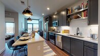 Located in Atlanta's prestigious 30305 corridor, this single-floor residence showcases a thoughtfully designed open-concept layout with modern finishes throughout. Rich hardwood flooring flows seamlessly across the main living areas, anchoring the cohesive contemporary aesthetic.

The kitchen is a standout feature, outfitted with slate-gray shaker cabinetry extending to the ceiling, a herringbone tile backsplash, light quartz countertops, and a full suite of stainless steel appliances including a gas range. A central island with pendant lighting in brushed brass and matte black serves as both a prep space and a dining area with bar seating.

The living room benefits from floor-to-ceiling glass doors that open onto a private balcony, flooding the space with natural light and offering open city views. The bedroom is a comfortable retreat with plush carpet, a large window framing outdoor views, and ample space for furnishings.

The bathroom features striking black-and-white patterned tile flooring, a dual-sink vanity with gray cabinetry, and white quartz countertops. A stacked in-unit washer and dryer adds everyday convenience. The overall ambiance is polished, modern, and well-appointed throughout.