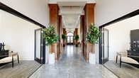Located at 1102 Mba Ct in Kannapolis, NC, this single-floor amenity space blends classic architectural character with modern interior design. The grand hallways set the tone immediately, framed by stately rich wood columns with decorative capitals, polished concrete floors that reflect the recessed lighting above, and lush fiddle-leaf fig trees that add a vibrant natural touch. Black-framed glass doors line the corridor, leading to distinct functional zones throughout the space.

The main lounge area is an open, airy gathering space anchored by a stone-clad fireplace with a wall-mounted television and flanking built-in shelving. White upholstered seating creates an inviting conversation area beneath soaring ceilings. Adjacent to the lounge is a sleek coffee bar and kitchenette, complete with counter seating and beverage stations, perfect for casual use.

A dedicated game room features a full-size billiard table set beneath oversized pendant lights, with wainscoted walls, bold artwork, and arched entry doors that echo the building's architectural charm. A professional workspace with a desk and seating offers a quieter setting for focused tasks. Coffered ceilings, arched windows, and consistently elegant finishes throughout create a cohesive, upscale ambiance across the entire space.
