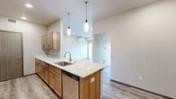 This well-designed two-bedroom, one-bathroom unit at 205 S Pines Rd in Spokane Valley, Washington offers a thoughtfully laid-out single-level floor plan with modern finishes throughout. The kitchen serves as a central highlight, featuring warm-toned light wood cabinetry, crisp white quartz countertops, stainless steel appliances including a refrigerator, electric range, and microwave, and a peninsula island with an undermount sink and pendant lighting overhead. Light luxury vinyl plank flooring runs throughout the kitchen and living areas, contributing to a clean, contemporary aesthetic.

The primary bedroom is a comfortable, carpeted retreat with a window offering natural light and outdoor views of surrounding greenery. A spacious walk-in closet with wire shelving provides generous storage. The second bedroom also features light LVP flooring and a sliding closet door. The bathroom includes a light wood vanity with quartz countertop and a large mirror. A wall-mounted mini-split system provides efficient climate control throughout the unit. Neutral white walls and modern hardware give the space a cohesive, move-in-ready feel.