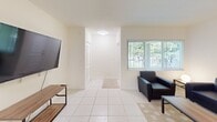 This well-appointed 1-bedroom, 1-bathroom apartment in Boca Raton offers 570 square feet of thoughtfully designed living space. The layout includes a spacious living room, a functional kitchen, and a generously sized 180 square foot bedroom. The living area is adorned with sleek tile flooring and features a large window that floods the space with natural light, complemented by a wall-mounted TV for entertainment. The kitchen boasts wooden cabinets, ample counter space, and essential appliances including a refrigerator and microwave. The bathroom is equipped with a tub-shower combination and a convenient towel bar. The bedroom accommodates a full-sized bed and includes a study area with a desk and dresser, illuminated by a wide window with vertical blinds. Throughout the apartment, neutral tones create a calm and inviting atmosphere, while the strategic placement of furniture maximizes the use of space. This compact yet comfortable apartment is ideal for those seeking a modern, low-maintenance living solution in a prime Boca Raton location.