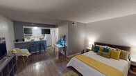 This single-floor studio unit offers a well-designed open-concept layout that efficiently integrates sleeping, living, and dining areas into one cohesive space. Rich hardwood-style flooring extends throughout the main area, complemented by textured ceilings and exposed painted brick accent walls that add architectural character.

The sleeping and living areas flow seamlessly together, with a full-sized bed positioned alongside a dedicated living space that includes a flat-screen TV and a glass door leading to an outdoor area, allowing natural light to fill the room.

The kitchen is a standout feature, showcasing dark navy cabinetry paired with white quartz countertops and a classic white subway tile backsplash. Equipped with a gas range, refrigerator, and ample storage, it also includes a peninsula with bar seating, making it ideal for casual dining.

A full bathroom includes a tub-shower combination, vanity with storage, and is styled with coordinating teal and gray chevron accents. Throughout the space, a contemporary color palette of gray, teal, and yellow creates a cohesive and inviting atmosphere, making this studio both functional and visually appealing.