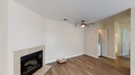 This single-story residence offers a cohesive, well-appointed layout with consistent neutral tones and modern finishes throughout. The living area is a comfortable, open space highlighted by a tile-surround fireplace, a ceiling fan with integrated lighting, and wood-style plank flooring that extends throughout the main living areas. A half-wall partition separates the living space from the kitchen, creating an open connection between the two areas without fully removing definition.

The kitchen is efficiently designed, featuring granite countertops, white cabinetry, and black appliances including an electric range and microwave. A window above the counter provides a pleasant view of the surrounding greenery, bringing in natural light. The kitchen connects to a laundry area with visible appliances tucked neatly behind louvered doors.

A sliding glass door in a secondary area of the unit opens to a private outdoor patio space, filling the room with natural light and offering exterior access. The bedroom is generously sized and finished with plush carpeting and a window with outdoor views, creating a calm and restful atmosphere. The bathroom features a white vanity with granite countertop, a large mirror, and wood-style flooring, maintaining the clean aesthetic found throughout the home.