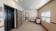 This single-floor residential unit offers a thoughtfully designed layout that balances comfort and functionality. The entry area welcomes residents and guests with neutral-toned walls, carpeted flooring, and a small seating arrangement featuring two upholstered chairs, creating a calm and inviting transition into the space.

The living area features light wood-style flooring and opens directly to a private balcony through a sliding glass door framed by vertical blinds, allowing natural light to fill the room and providing pleasant outdoor views of a green landscape. A cozy dining nook nearby accommodates a round bistro-style table with wrought iron chairs, accented by decorative travel-themed wall art that adds personality to the space.

The kitchen is efficiently organized with rich dark wood cabinetry, stainless steel appliances including a refrigerator, range, and microwave, along with a breakfast bar that connects seamlessly to the living area. Light wood-style flooring continues throughout, maintaining visual consistency.

The bedroom, visible through a doorway, offers carpeted flooring and a quiet, restful ambiance. Throughout the unit, warm neutral tones, recessed and flush-mount lighting, and practical finishes create a cohesive and comfortable living environment.