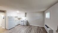 This single-floor unit offers a straightforward, functional layout designed for comfortable everyday living. The open-concept living and kitchen area is unified by durable wood-look laminate flooring in a neutral grey-brown tone, creating a cohesive and easy-to-maintain interior throughout.

The kitchen is efficiently arranged in an L-shaped configuration and includes white cabinetry with ample upper and lower storage, light granite-style countertops, a double stainless steel sink, a white electric coil range, and a full-size white refrigerator. Under-cabinet lighting provides added visibility for meal preparation.

The living area is bright and open, featuring two windows fitted with blinds that allow natural light to filter in, along with a wall-mounted PTAC heating and cooling unit for year-round climate control. A white entry door with a sidelight panel provides direct access to the unit.

The bedroom is a quiet, well-proportioned room with wood-look flooring and a window offering natural light. Neutral wall tones throughout the unit contribute to a calm, clean aesthetic.

The bathroom is equipped with a full-size soaking tub and shower combo featuring a white surround and chrome fixtures, maintaining the unit's clean and functional character. Overall, the space presents a neat, move-in-ready environment with a practical and cohesive design.