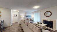 This single-floor, two-bedroom, two-bathroom residence at Magnolia in Memphis, Tennessee offers a well-organized layout designed for functional and comfortable living. The living room serves as the central gathering space, featuring wood-style flooring, a textured ceiling, and a tiled fireplace as a focal point. Vertical blinds cover a sliding glass door that connects the interior to the outdoors, allowing natural light to filter in. The kitchen is equipped with white cabinetry, black appliances, and a granite-topped breakfast bar that provides additional prep and seating space, with wood-style flooring continuing throughout. An adjacent dining area completes the open feel of this shared space. The primary bedroom is carpeted and bright, benefiting from a window with natural light and ample room for full-sized furniture. The second bedroom is similarly carpeted and includes a ceiling fan with light fixture and its own window overlooking greenery. Both bathrooms feature tub-shower combinations with white tile surrounds. One bathroom includes a granite vanity countertop with wood-style flooring, while the second offers a clean, neutral finish. Throughout, the unit maintains a cohesive, neutral color palette.
