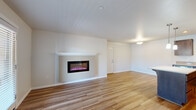 This single-floor residence offers a thoughtfully designed layout that balances comfort and functionality. The open living area serves as the centerpiece of the space, highlighted by a wall-mounted electric fireplace with a sleek white mantel that adds a contemporary focal point. Wood-look flooring extends throughout the main living areas, lending a warm, cohesive aesthetic. A sliding glass door with an adjacent window opens to a private balcony, filling the space with natural light and offering outdoor views.

The kitchen is well-appointed with rich, dark wood cabinetry providing ample storage, light countertops, and a full suite of stainless steel appliances including a refrigerator, range, built-in microwave, and dishwasher. Recessed lighting and a pendant fixture illuminate the workspace, which also features a central island for additional prep space.

The bedroom is finished with plush carpeting and receives natural light through a window fitted with blinds. A wall-mounted mini-split unit provides dedicated climate control. The bathroom is clean and functional, featuring a full tub-shower combination with white surround and brushed nickel grab bars. Throughout, the neutral color palette and consistent finishes create a modern, move-in-ready environment.